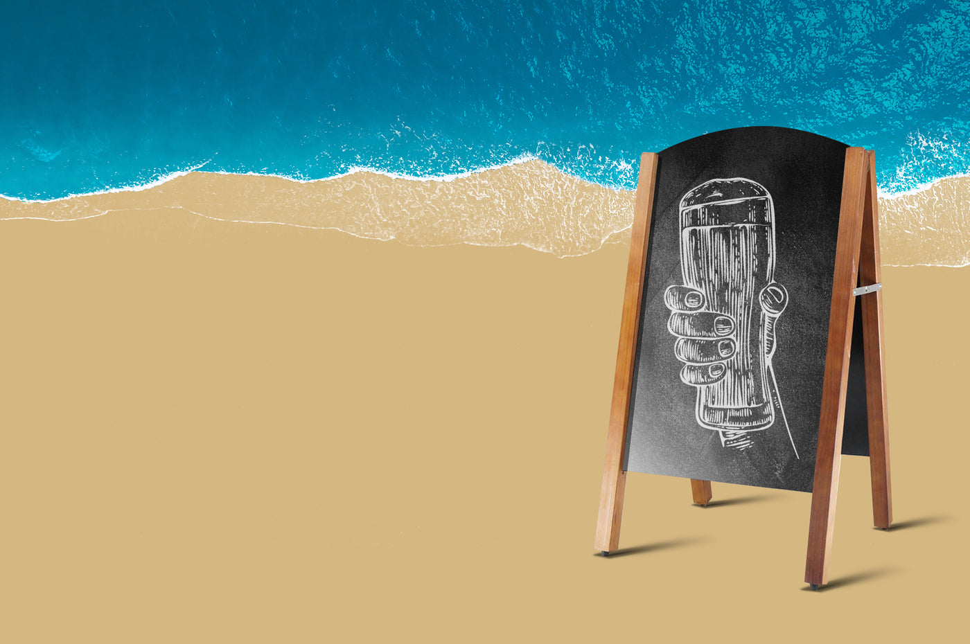 Chalk board with craft beer glass in a hand with the ocean in the background.